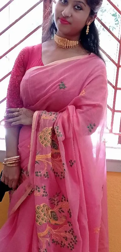 Woman in pink sari posing elegantly by a window.