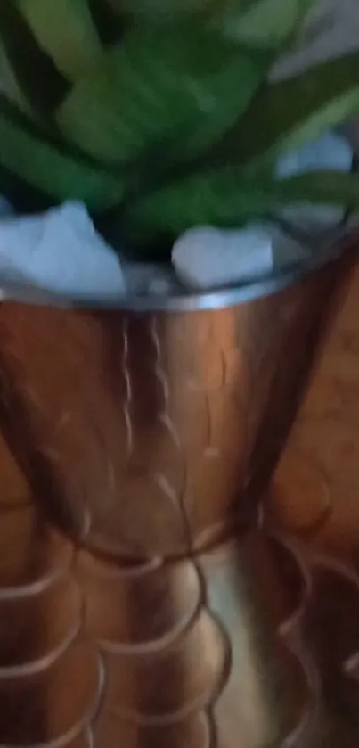 Elegant green plant in a metallic vase on a copper surface.