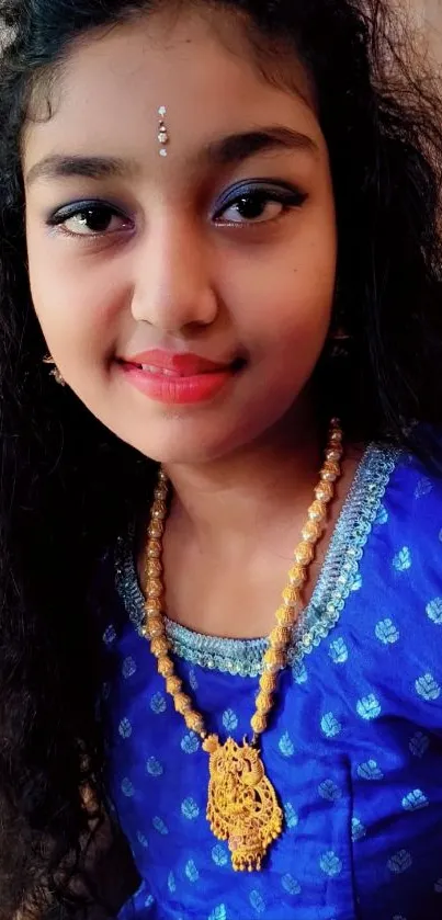 Portrait of a young woman in blue attire with gold jewelry, smiling gracefully.