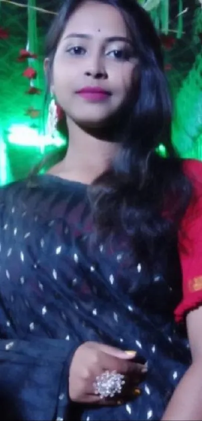 Woman in black saree at festive event with green and gold decor.