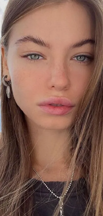 Elegant portrait of a woman with blue eyes and soft brown hair against a sky background.