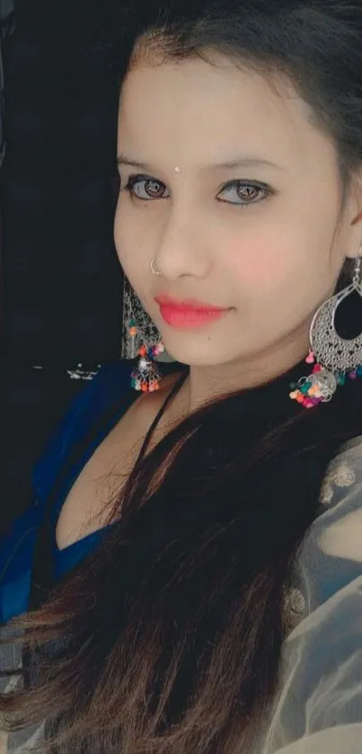 Woman in elegant portrait with intricate earrings and deep blue attire.