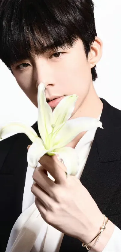 Portrait of a person in a black suit holding a white lily flower.