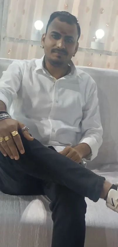 Man in white shirt seated elegantly on white sofa.