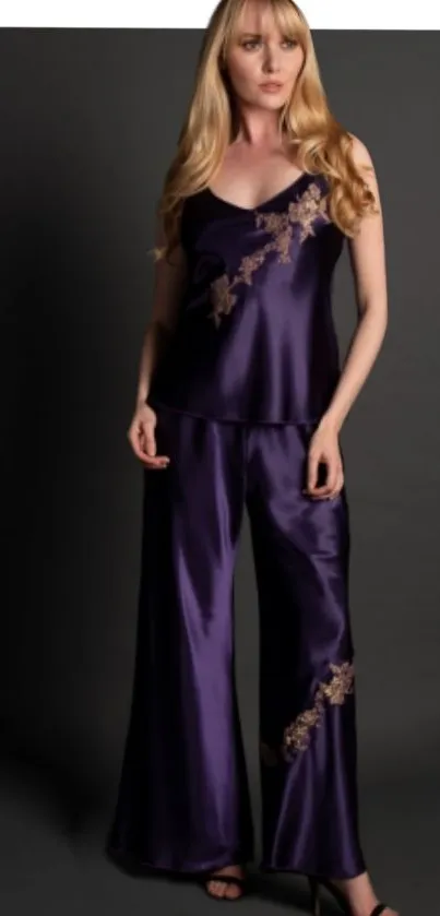 Woman in elegant purple satin pajamas on dark background.