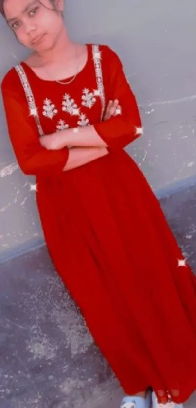 Young girl in an elegant red dress posing gracefully against a wall.