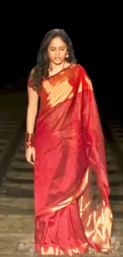 Woman in red saree on railway tracks at night.