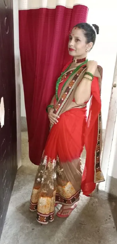 Woman in red saree standing by doorway with vibrant design.