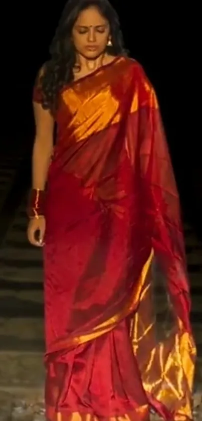 Woman in a red sari standing on train tracks with a dark background.