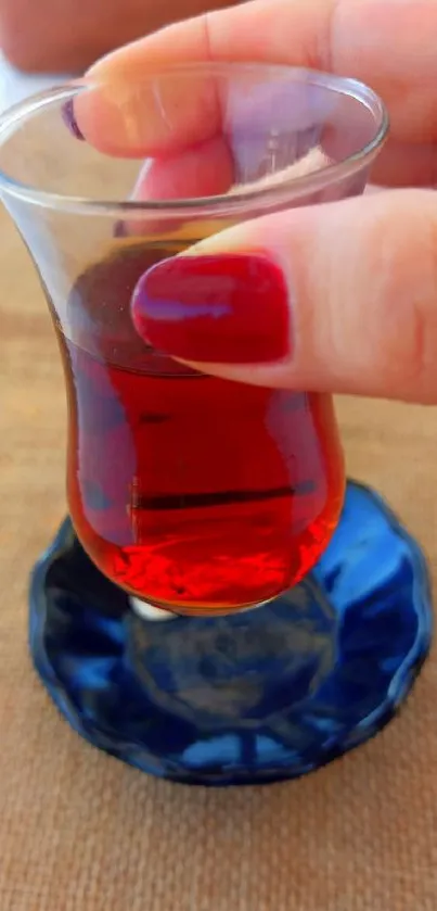 Red tea in glass cup with hand, on rustic table.