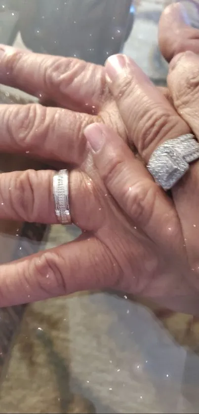 Hands adorned with sparkling diamond rings on a glass surface.