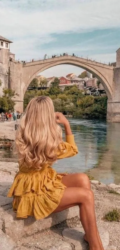 Woman in yellow dress by scenic river bridge.