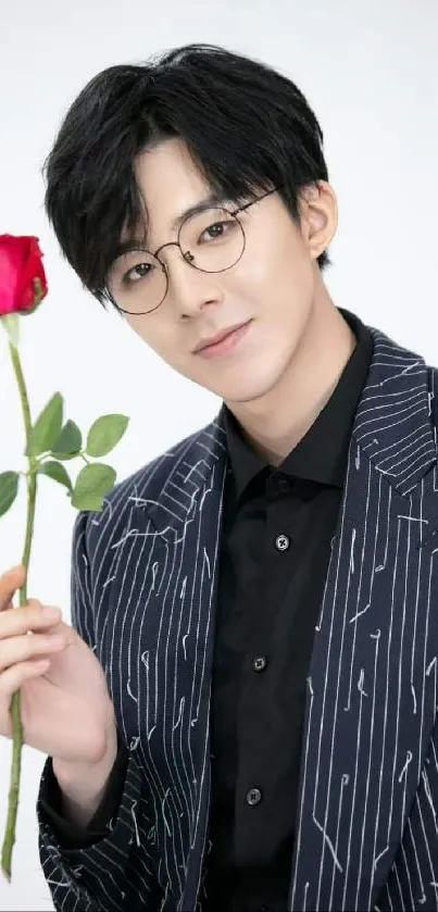 Man in glasses holding a red rose in a dark pinstripe suit.