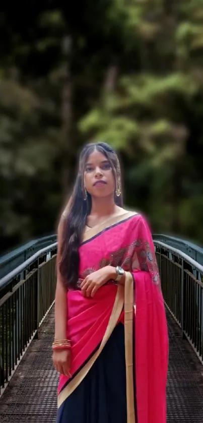 Woman in pink saree on a bridge with forest background.