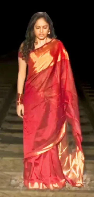 Woman in a red sari standing on a railway track at night.