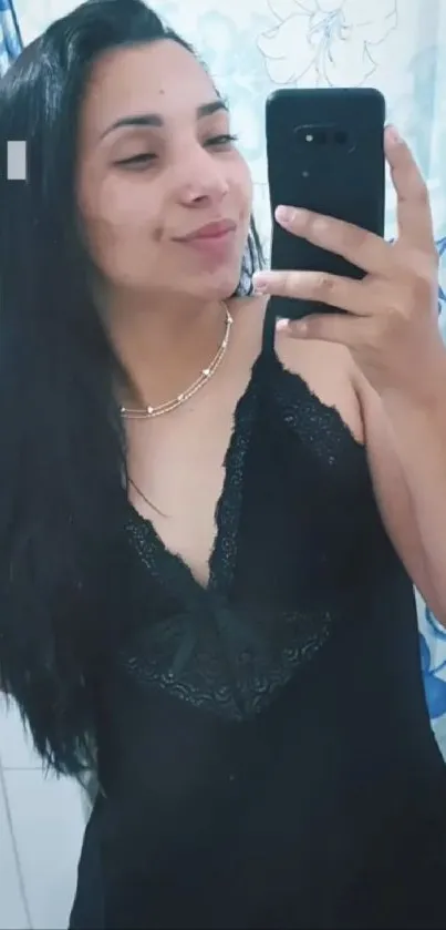 Woman in black dress taking mirror selfie.