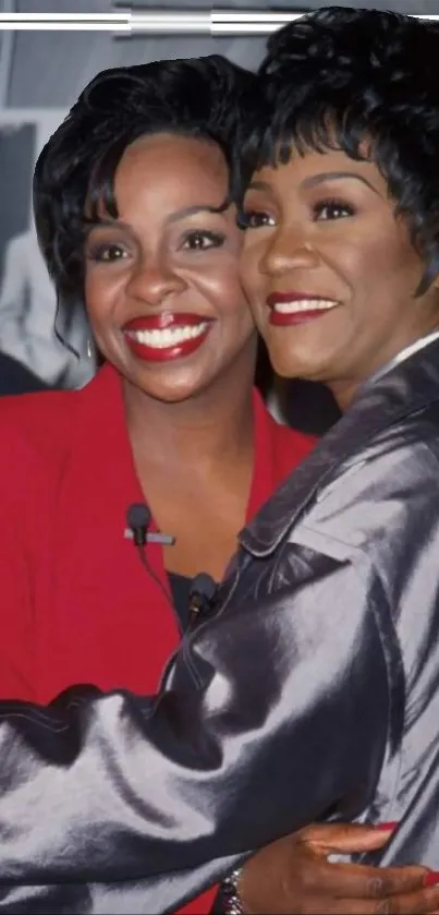 Two women smiling and embracing in stylish outfits.