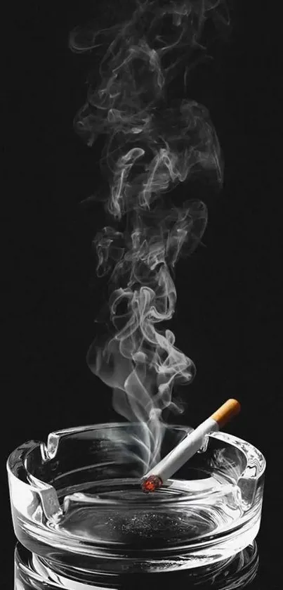 Smoke rising from a lit cigarette in a clear ashtray against a black background.