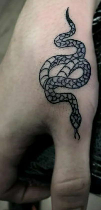 Hand with elegant black snake tattoo in artistic design.