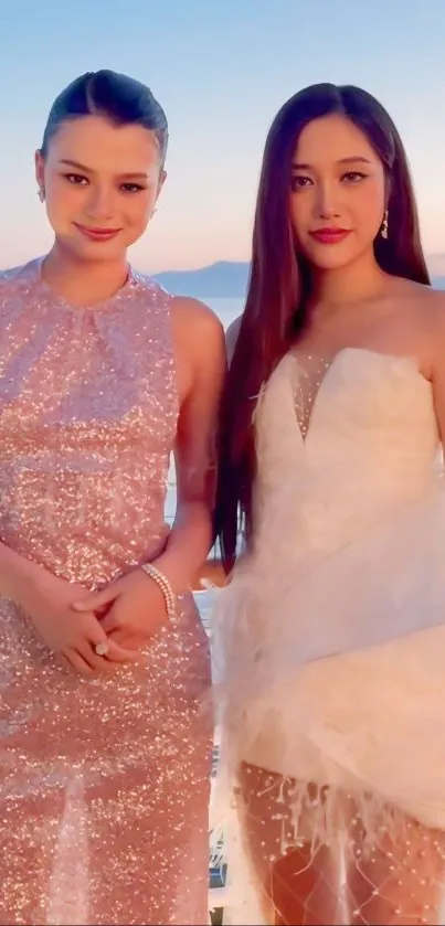 Two women in elegant dresses at sunset beach.