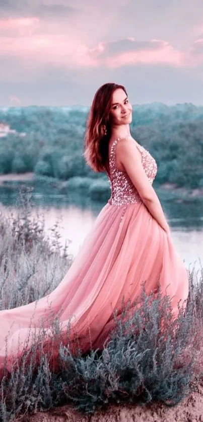 Woman in elegant pink gown by scenic sunset river.