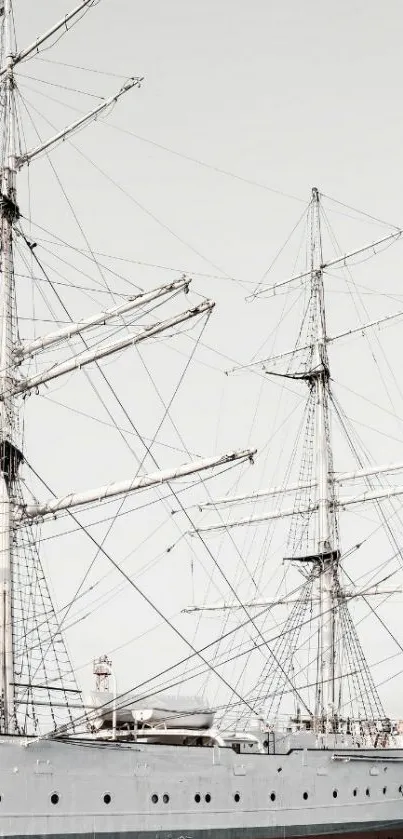 Mobile wallpaper featuring a tall ship with intricate rigging against a light gray sky.