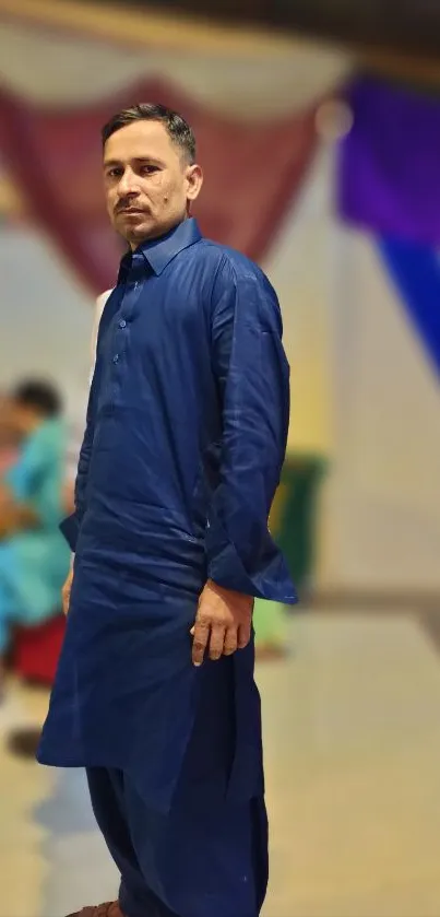 Man in blue traditional attire standing elegantly in vibrant setting.