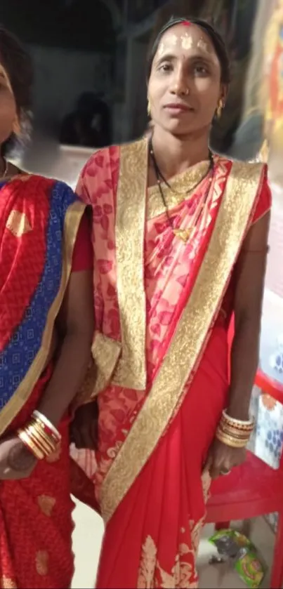 Women in vibrant red traditional sarees with golden embellishments.