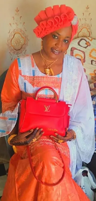 Woman in vibrant traditional attire holding a red handbag, seated elegantly.