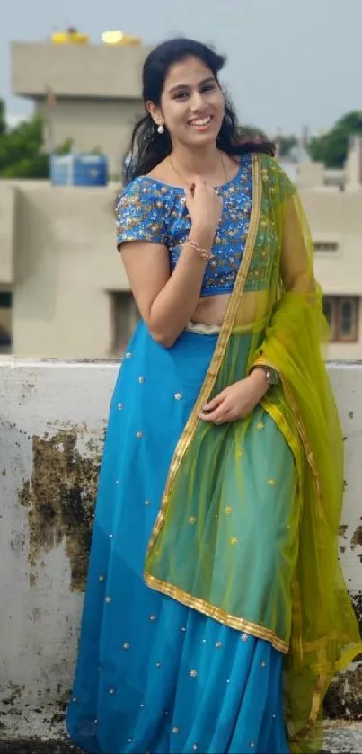 Woman in vibrant blue and green traditional attire on rooftop.