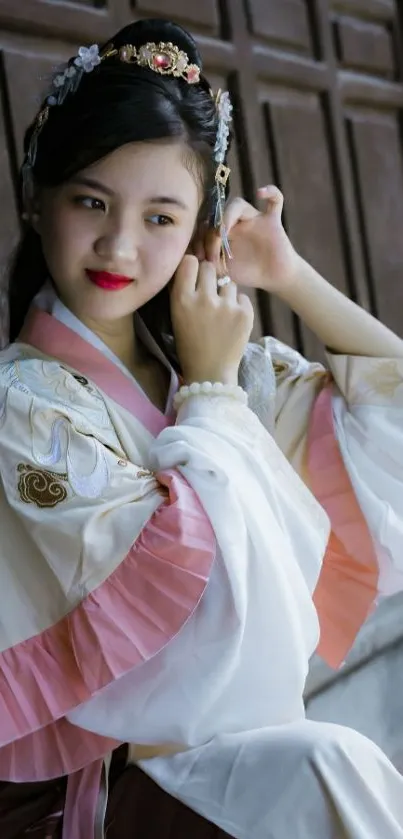 Girl in elegant traditional attire leaning against wooden background.