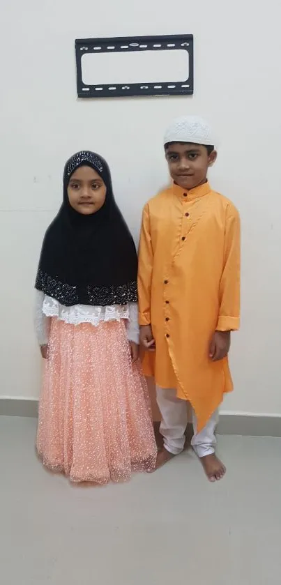 Two children in elegant traditional attire against a neutral background.