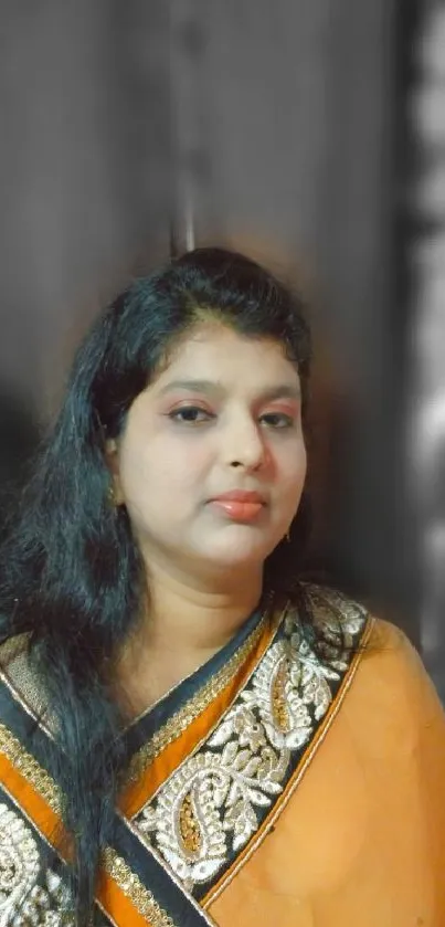 Portrait of a woman in a golden and orange sari against a blurred background.