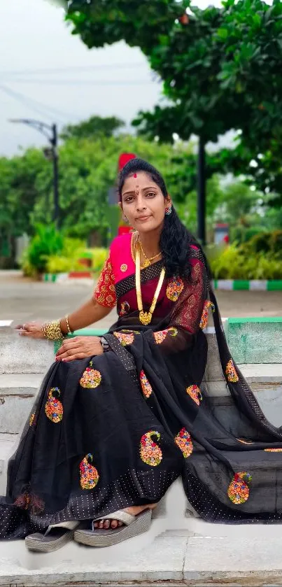 Woman wearing black saree sitting outdoors.