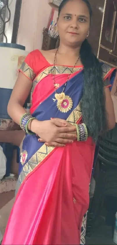 Woman in a red and gold saree posing gracefully indoors.