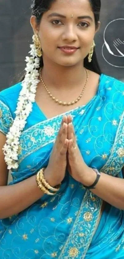 Woman in traditional blue sari with gold designs, hands clasped gracefully.