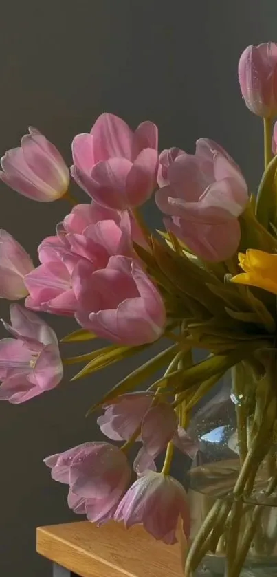 Pink and yellow tulips in a vase on a wooden table.