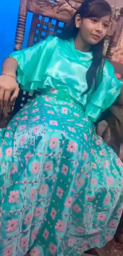 Girl in a turquoise floral dress relaxing in a wooden chair.