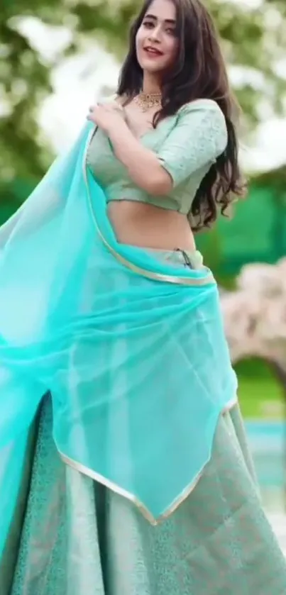 Woman wearing a turquoise saree with lush green background.