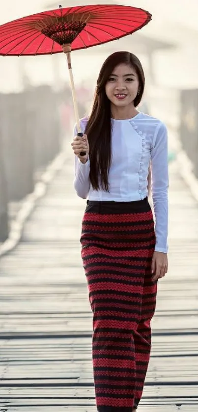 Woman in traditional dress with red umbrella on wooden path.