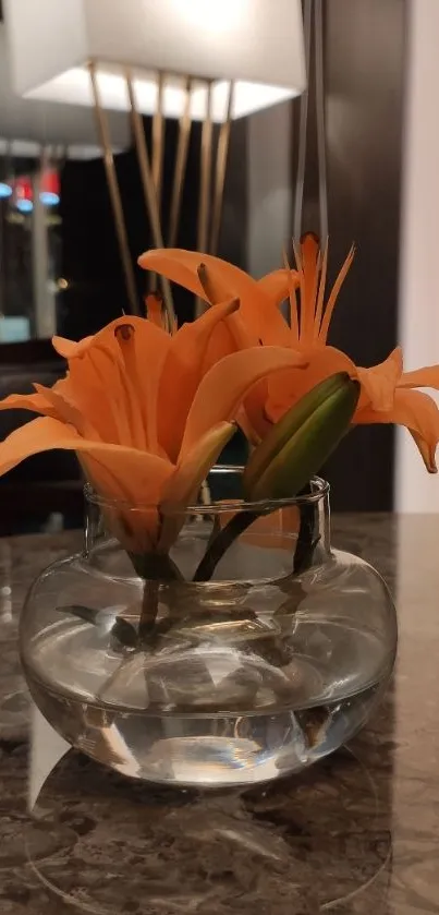 Orange flowers in a glass vase on a marble table.