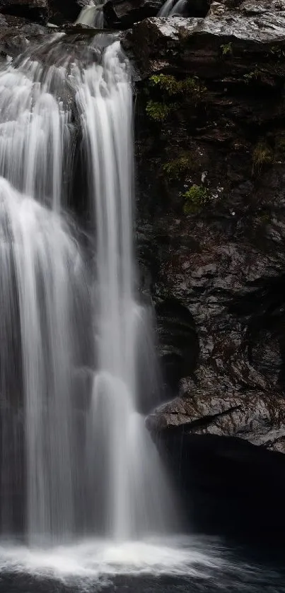 Serene waterfall cascading over rocks in a dark, tranquil setting with greenery.