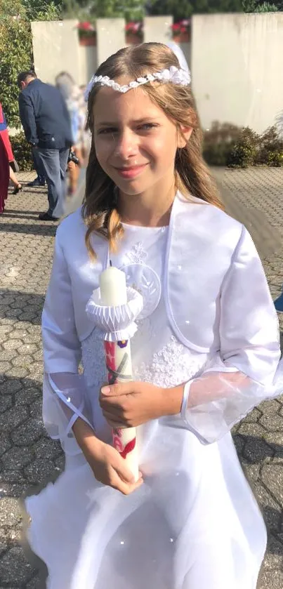 Girl in white dress holding candle at outdoor event.