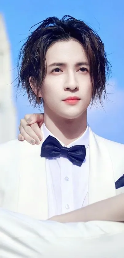 Man in white suit with bow tie against blue sky.