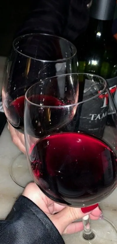 Elegant wine glasses clinking over a table, with a bottle in the background.