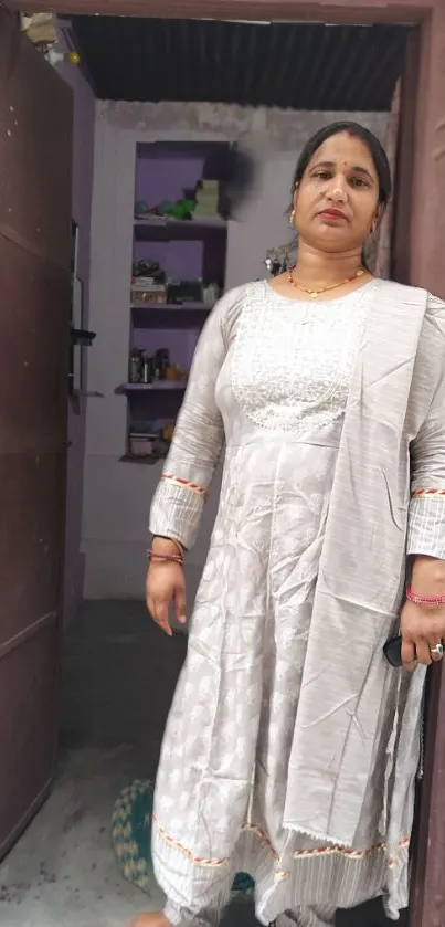 Woman in a grey outfit standing in a doorway with traditional elegance.