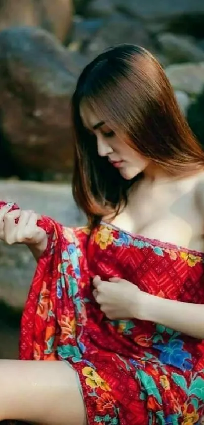 Woman in red dress sitting on rocks by the river, showcasing elegance and style.