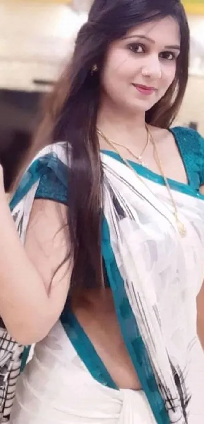 Elegant woman in a white saree with teal accents, posing gracefully.