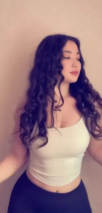 A serene woman with curly hair in a white top and black skirt against a beige background.