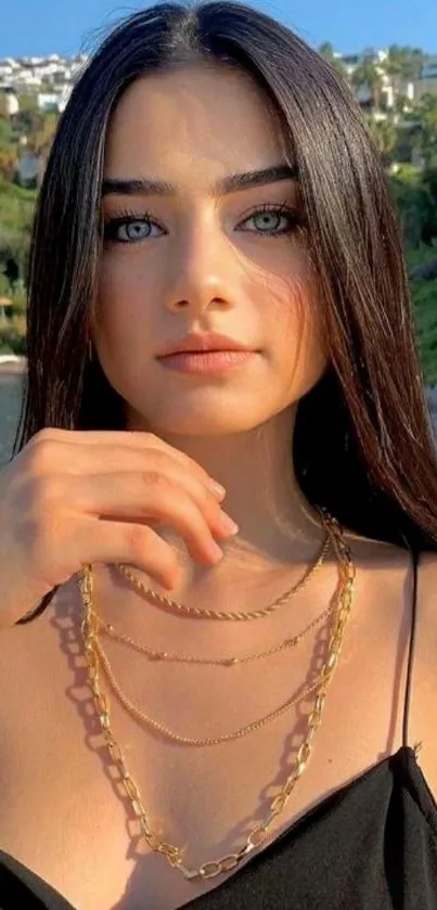 Elegant woman with blue eyes in a natural background, wearing a gold necklace.